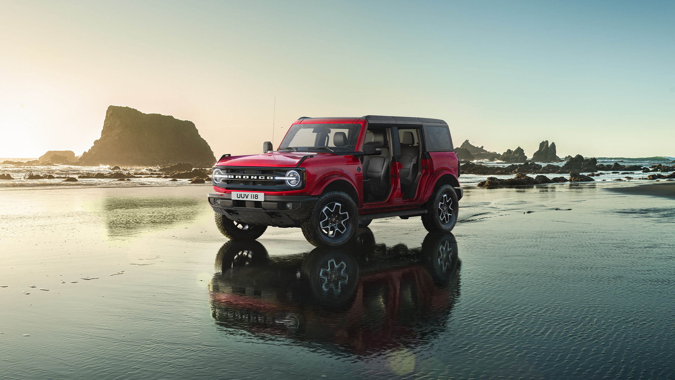 Ford Bronco in Rot, in 3/4-Frontansicht in felsiger Landschaft durch einen Wasserlauf fahrend