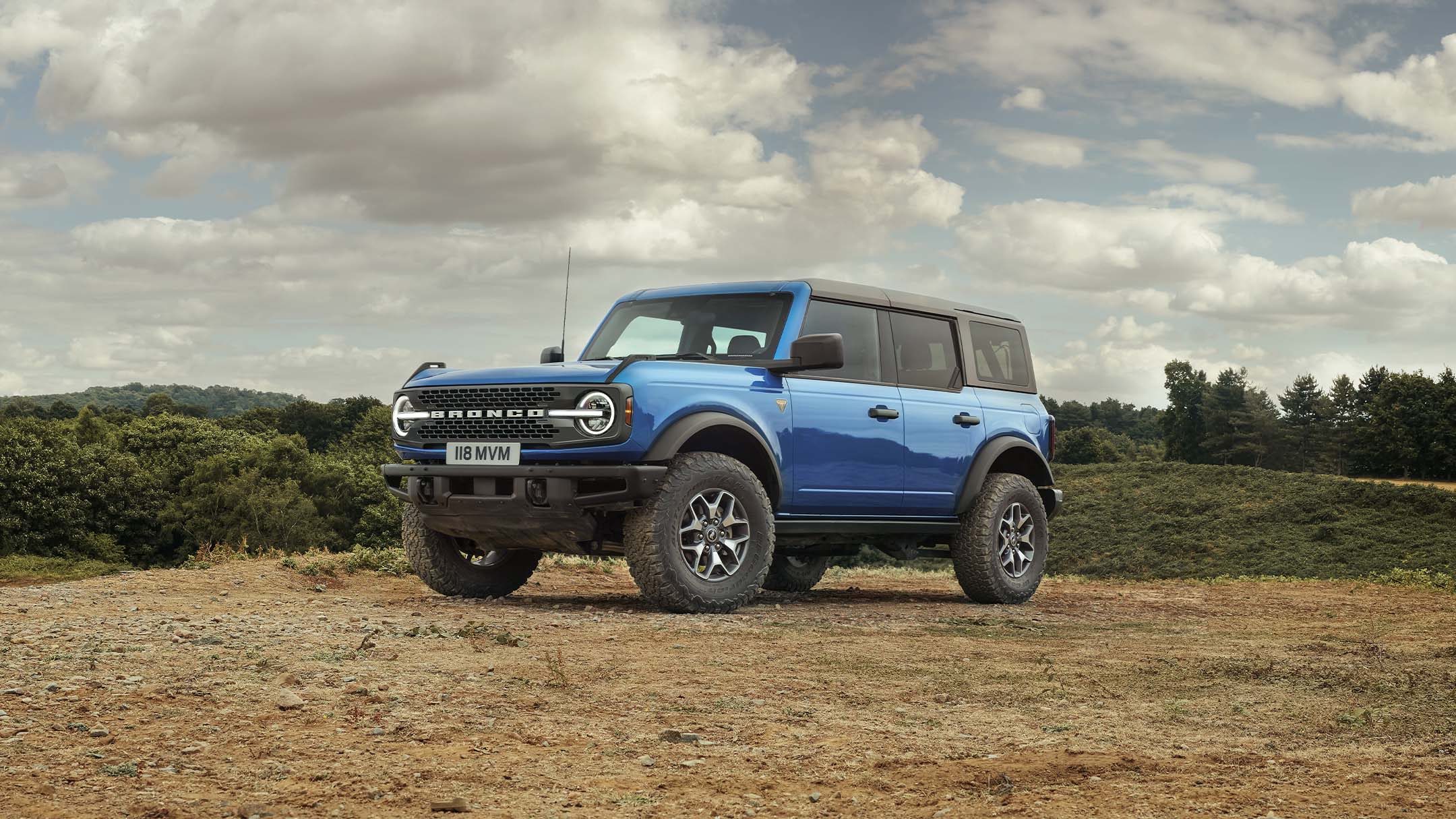 Ford Bronco in Blau, in 3/4-Frontansicht auf sandigem Untergrund stehend