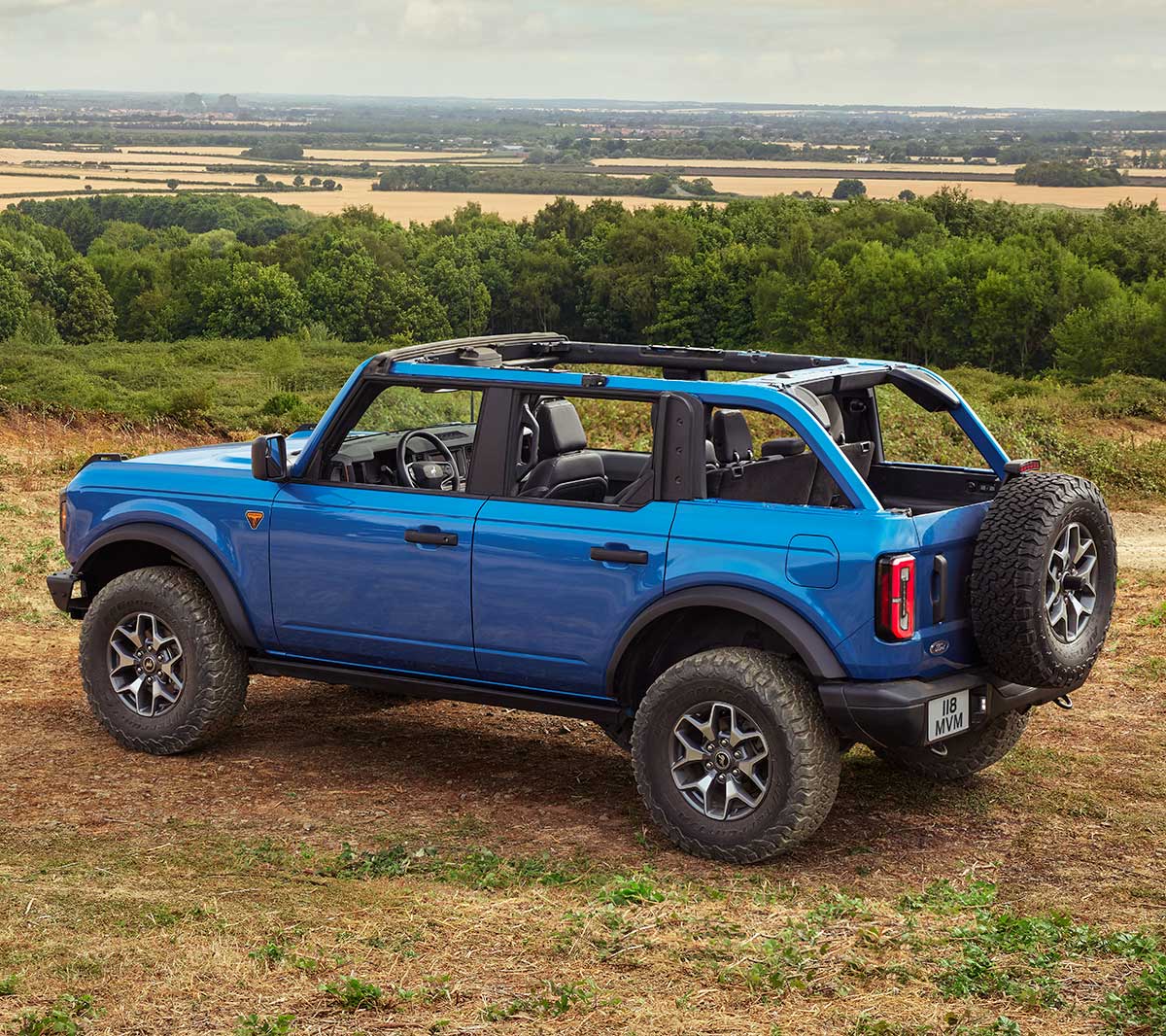 Ford Bronco in Blau, in 3/4-Rückansicht auf sandigem Untergrund fahrend